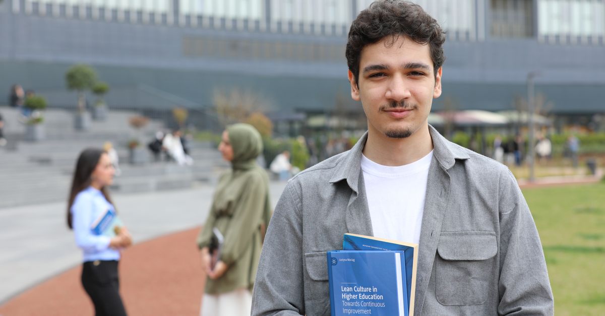A young adult student stands outside on campus holding textbooks, symbolizing education.